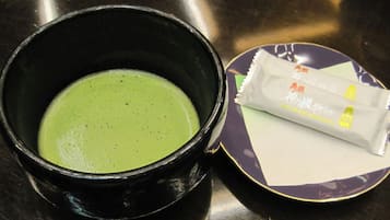 A black bowl with a green liquid, a purple plate with a white packet, and a spoon.