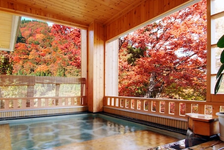 A wooden spa with a hot spring, wooden railings, and a view of autumn foliage.