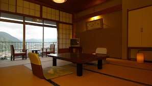 A traditional Japanese room with tatami flooring, a low table, chairs, a television, and a view of mountains. - Takahan (Yuzawa)