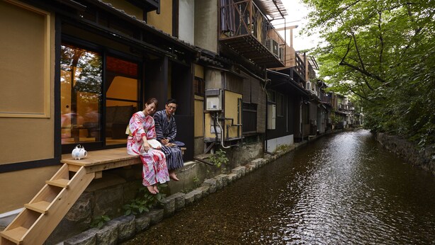 A narrow waterway flanked by traditional buildings with wooden steps leading down to the water. - Rinn Shijo Takasegawa (Kyoto)