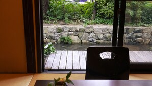 A view through a window of a stone wall and a wooden deck, with a small plant on a table. - Rinn Shijo Takasegawa (Kyoto)
