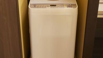 A compact, white, wall-mounted washer and dryer unit in a corner with a wooden door frame and a yellow wall.