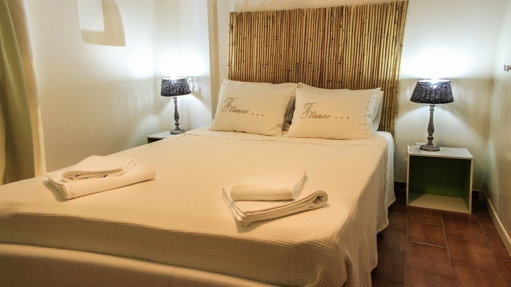 A neatly made bed with folded towels, two bedside tables with lamps, and a bamboo headboard.