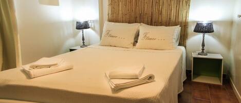 A neatly made bed with folded towels, two bedside tables with lamps, and a bamboo headboard.