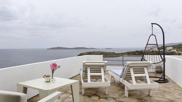 Una terrazza con mobili bianchi, una poltrona sospesa e vista sul mare e sulle isole.