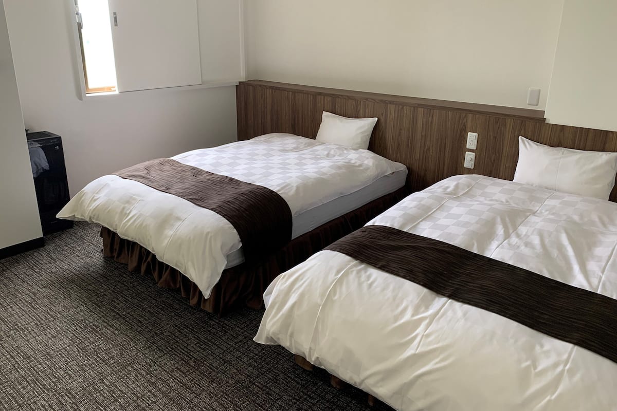 A hotel room with two beds, a wooden headboard, a small desk, and a window.