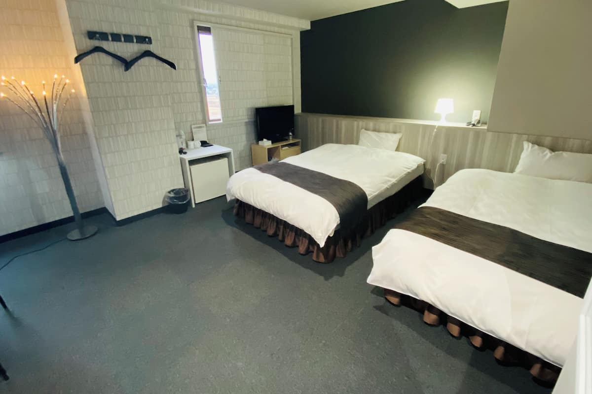 A hotel room with two beds, a desk, a TV, and a window.