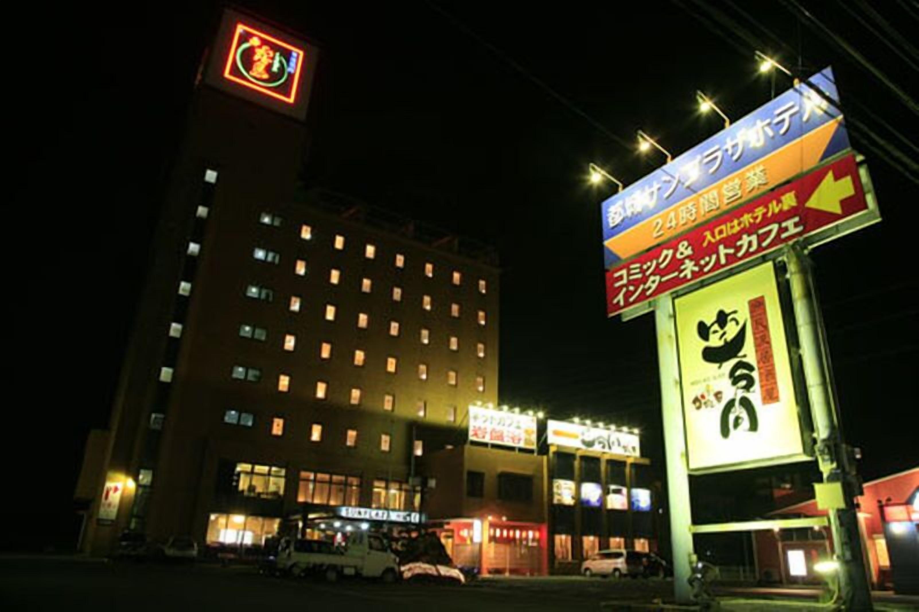 A hotel with multiple floors, illuminated signs, and a parking area with cars.