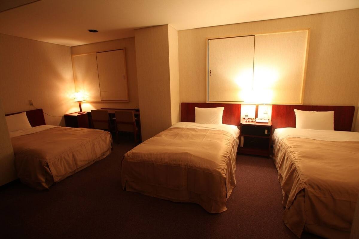 A hotel room with two single beds, a desk, and a chair.