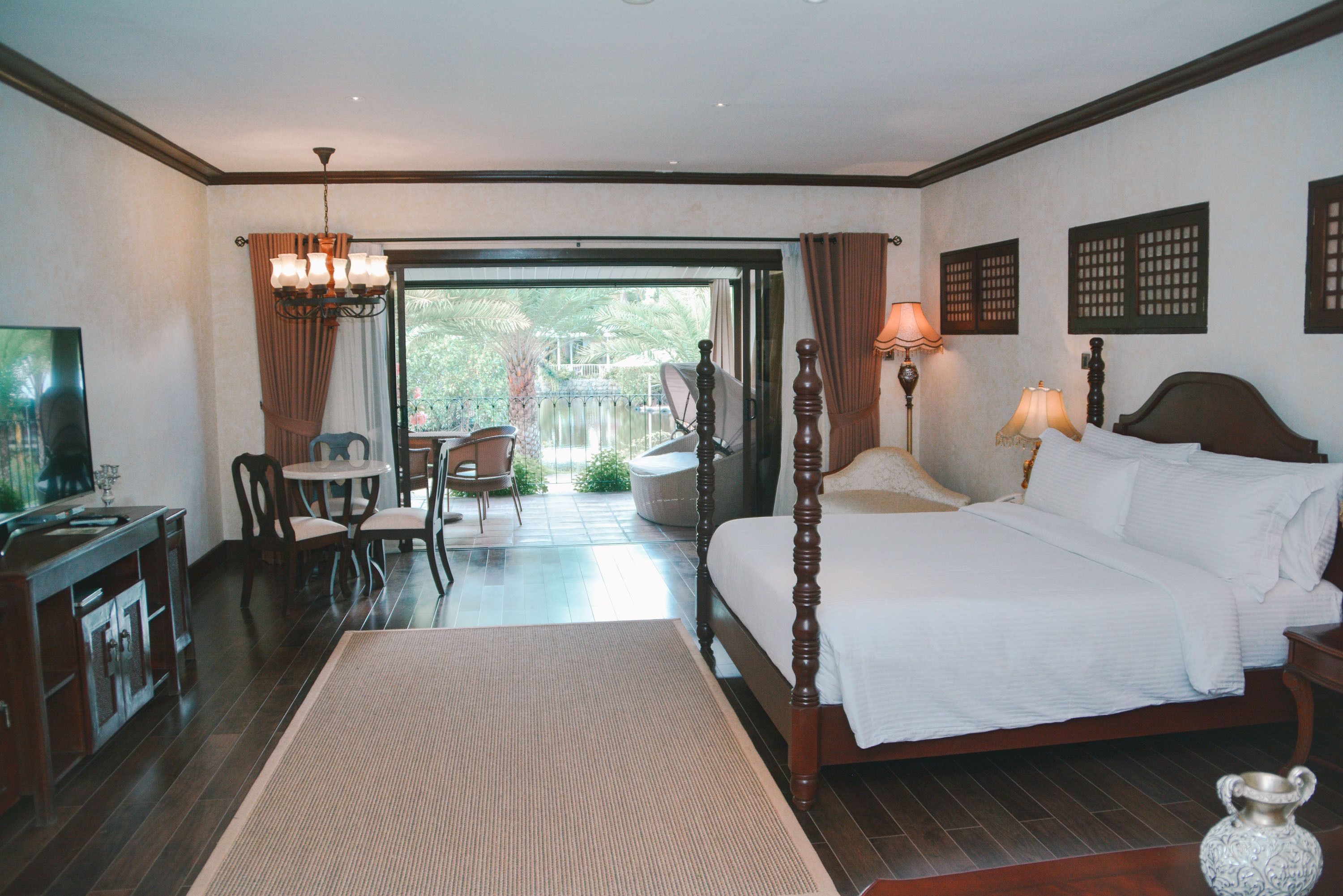 Habitación de hotel con una cama grande, un escritorio con televisor, un comedor con sillas y vistas al exterior.