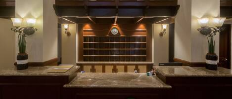 A hotel reception area with marble counters, wall-mounted clocks, and decorative wall sconces.