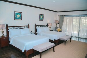 A hotel room with two beds, a bench, and a large window with curtains.