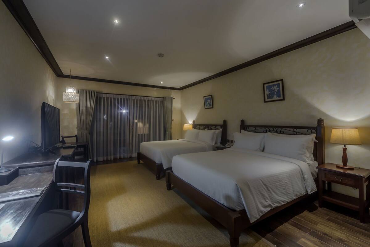 Una habitación de hotel con dos camas, un escritorio, un televisor y una lámpara de escritorio.