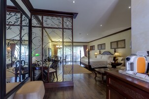 A hotel room with a dining area, a bed with a nightstand, a coffee maker, and a decorative screen.