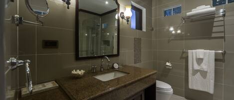Un baño moderno con lavamanos de granito, un espejo grande, inodoro y cabina de ducha de vidrio.