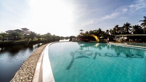 Una piscina cristalina con un tobogán acuático, rodeada de palmeras y edificios.
