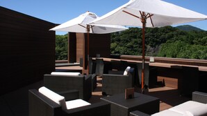 An outdoor seating area with wicker furniture and white umbrellas, overlooking a forested hillside. - Atagawa Prince Hotel (Higashiizu)