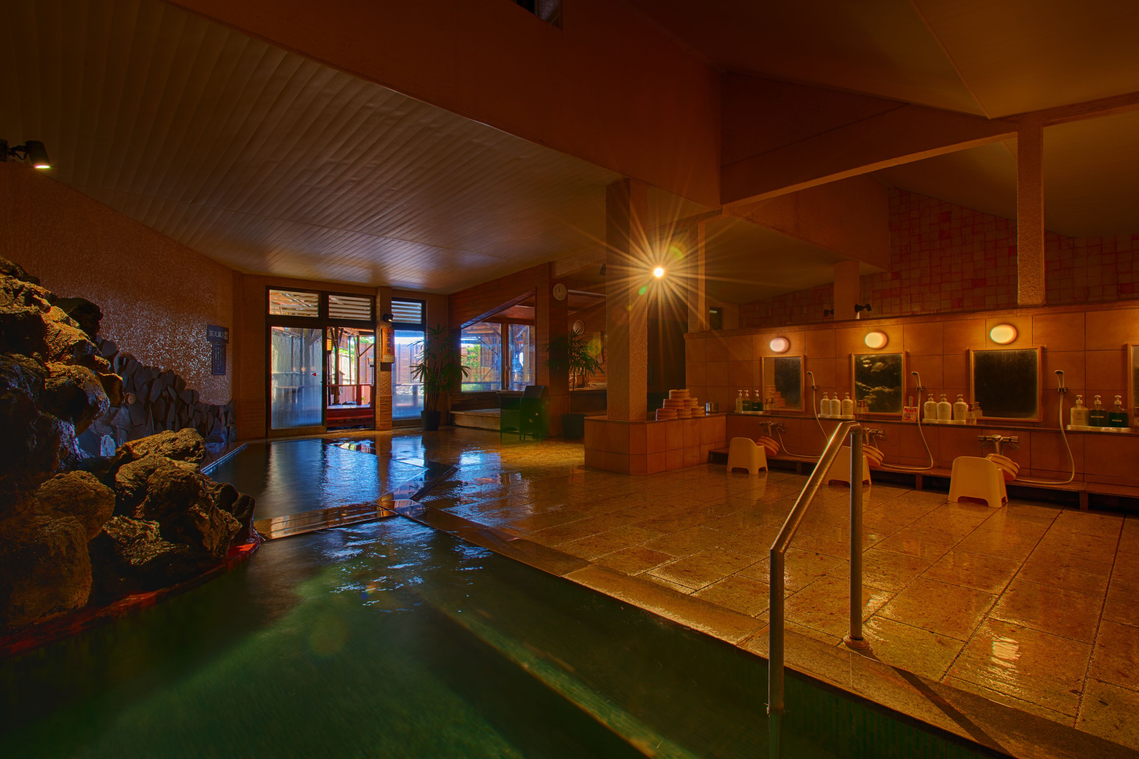 Zona de piscina húmeda con pared de piedra, mostrador de recepción y escalera que lleva a un nivel superior.