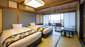 A hotel room with two beds, a sitting area with a bench, and a view of the outside through large windows. - Atagawa Prince Hotel (Higashiizu)