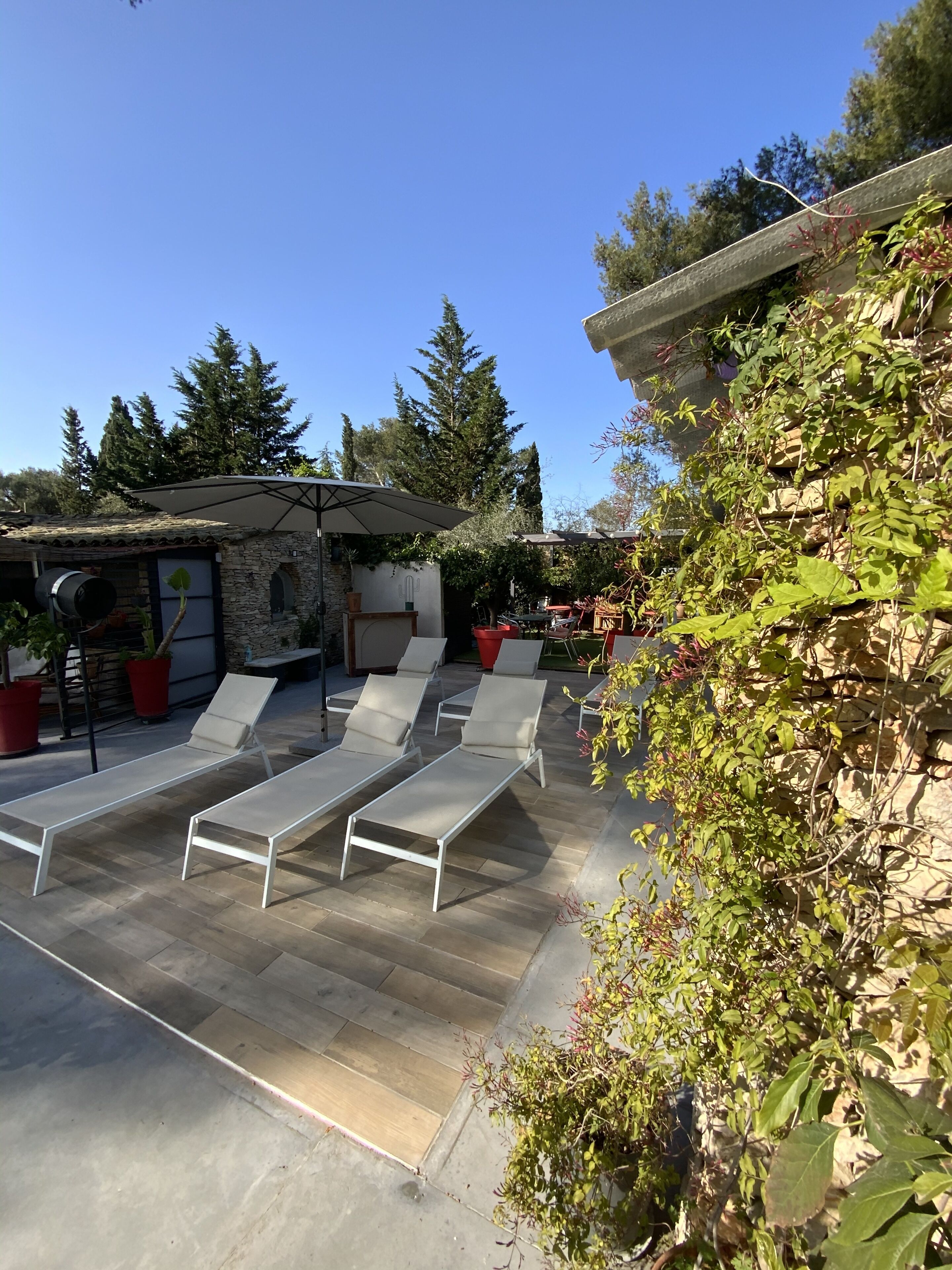 A patio with sun loungers, a stone building, and potted plants.