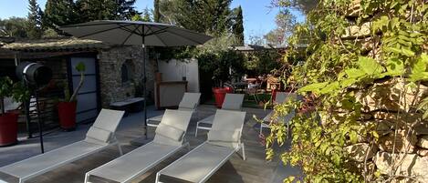 A patio with sun loungers, a stone building, and potted plants.