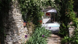 A stone building with a wooden pathway leading to a covered area with a bench. - Inn4bears (Nîmes)