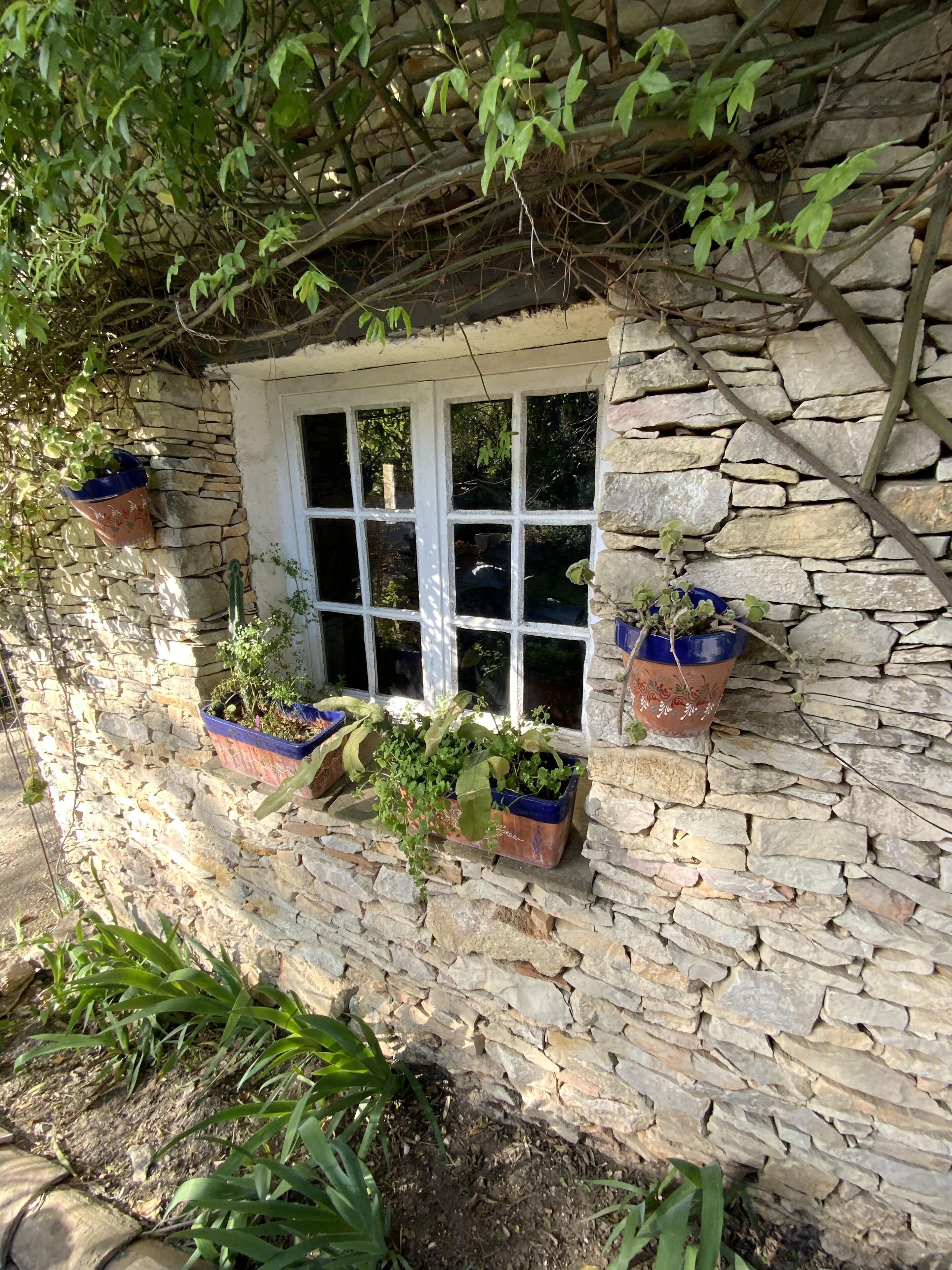 A stone wall with a window and potted plants.