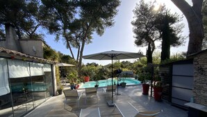 A poolside area with lounge chairs, a table, and a large umbrella. - Inn4bears (Nîmes)