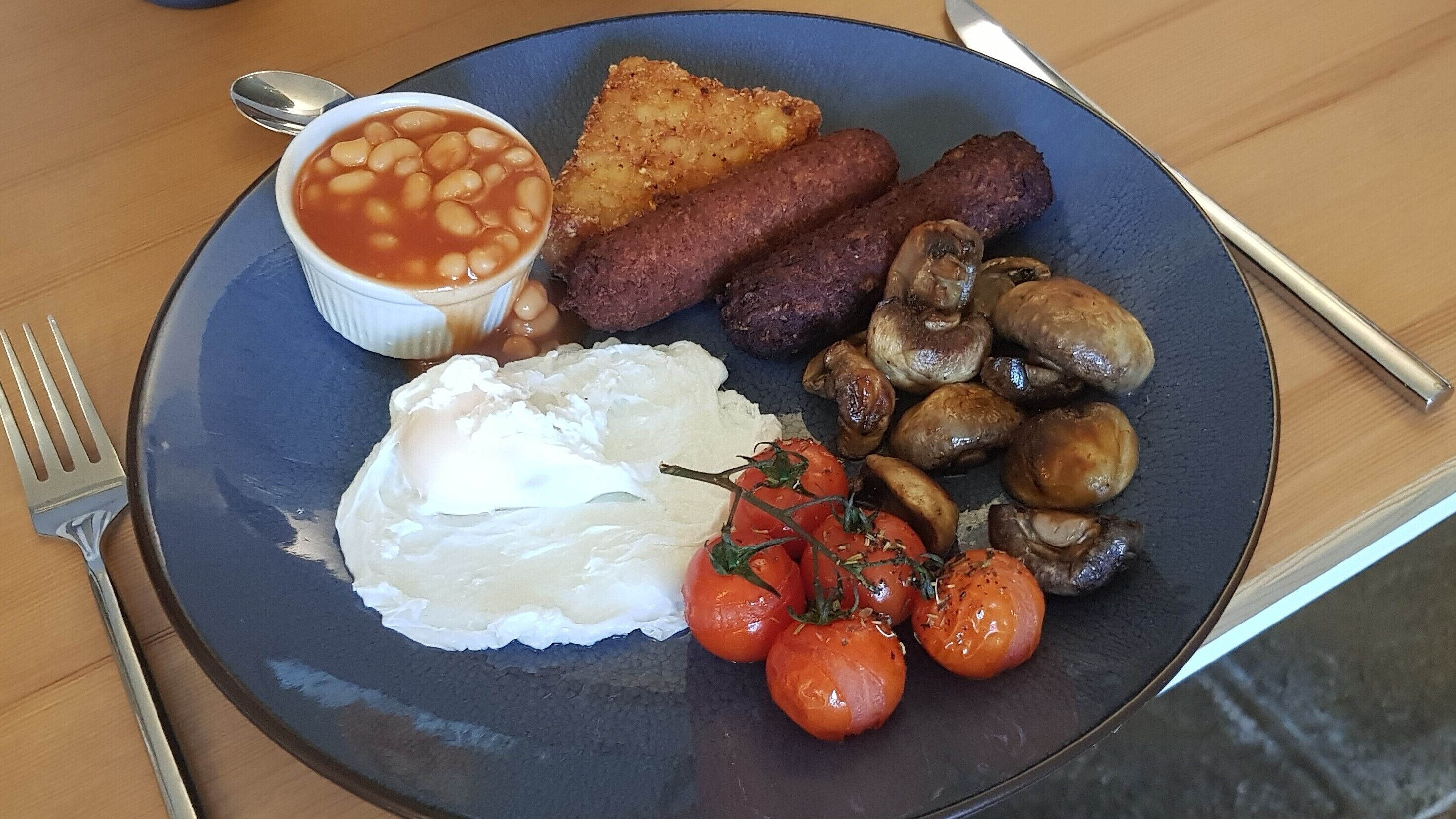 Un plato con frijoles, tostadas, salchichas, champiñones, huevos y tomates.