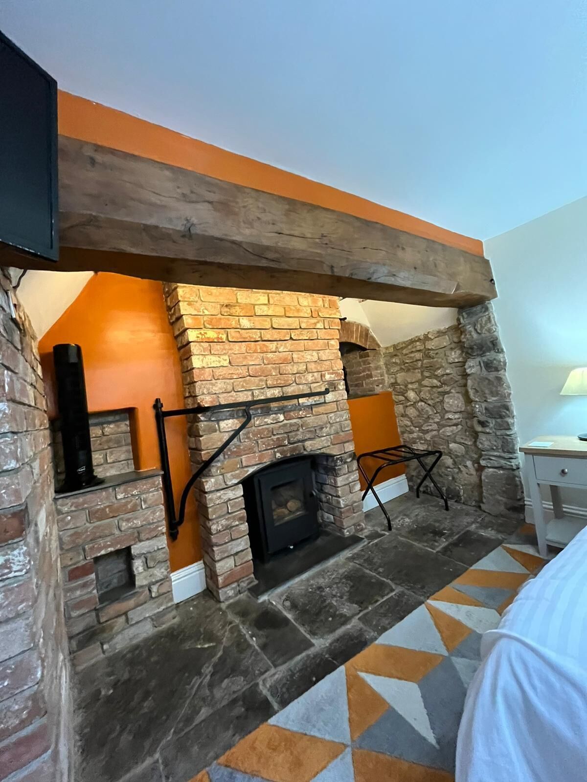 A room with a stone fireplace, a wooden ceiling beam, and a patterned floor.