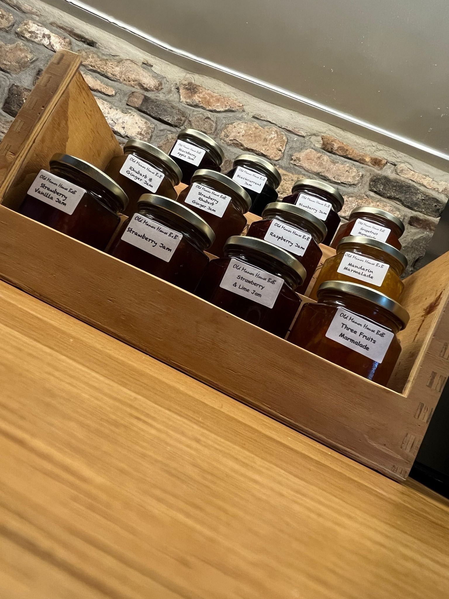 A wooden display case containing various jars of homemade jams with labels.