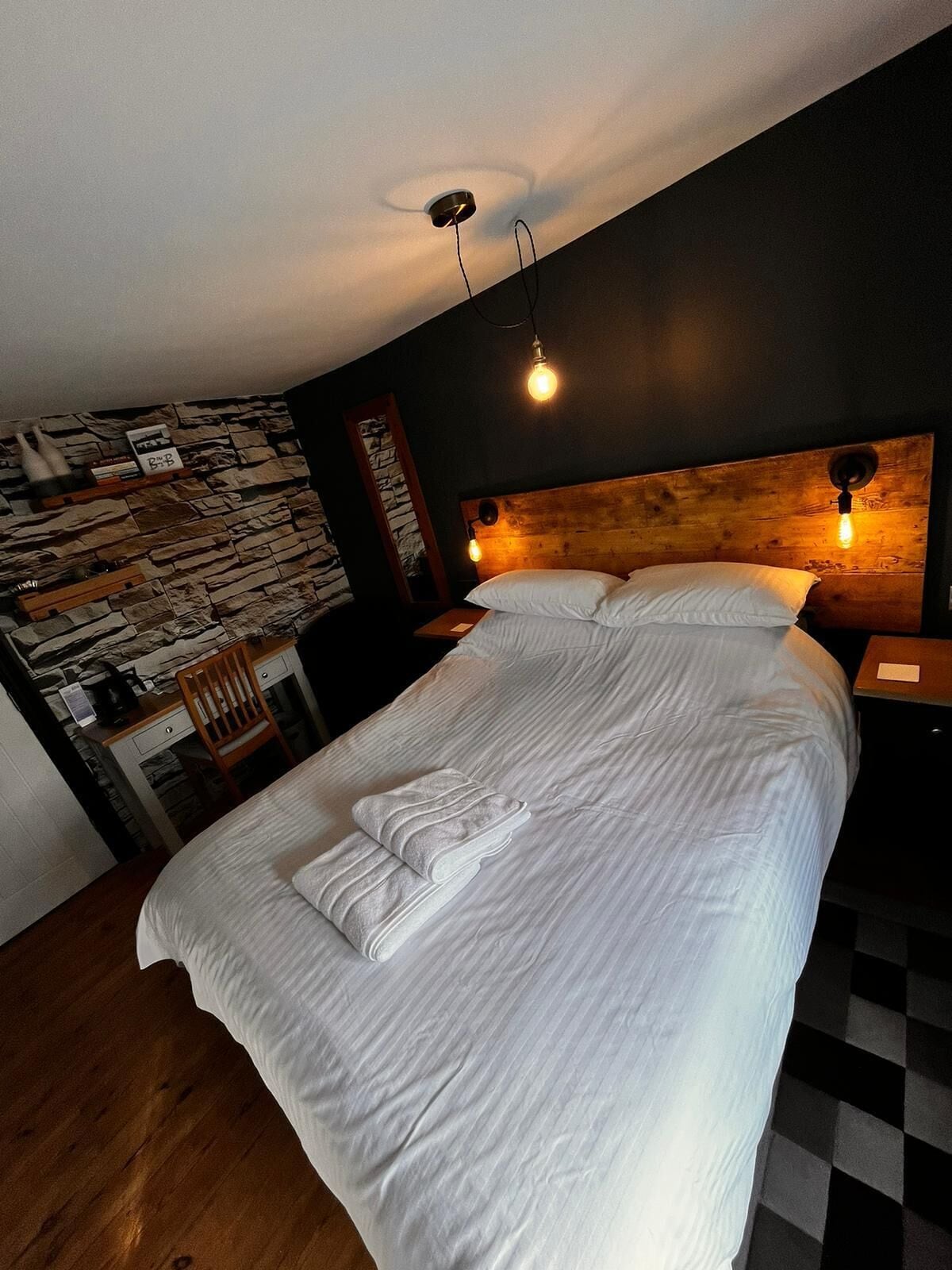 A neatly made bed with white linens and towels, a wooden headboard, and two wall-mounted light fixtures.
