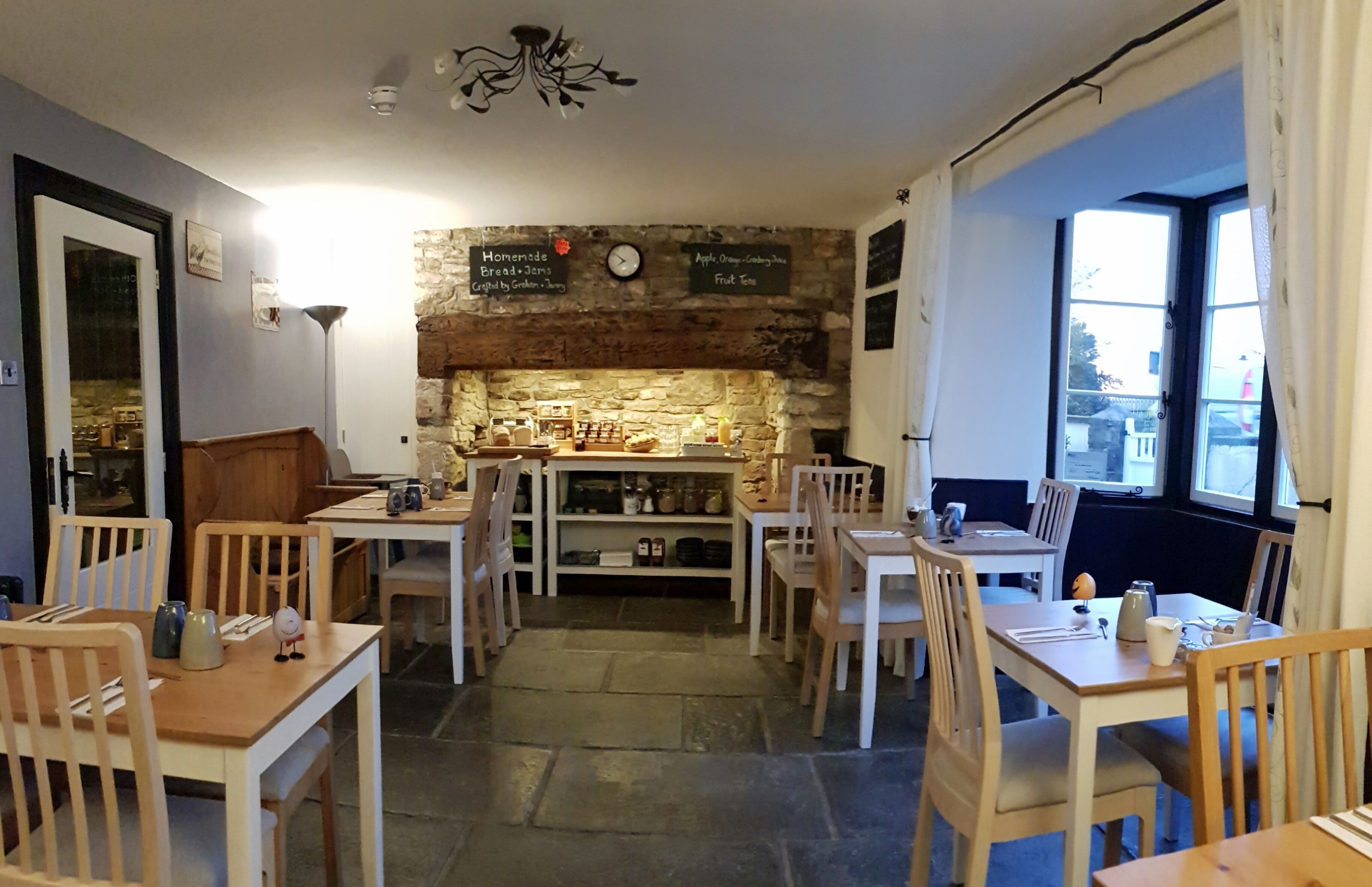 A cozy cafe with wooden tables and chairs, a stone wall, and a chalkboard menu.