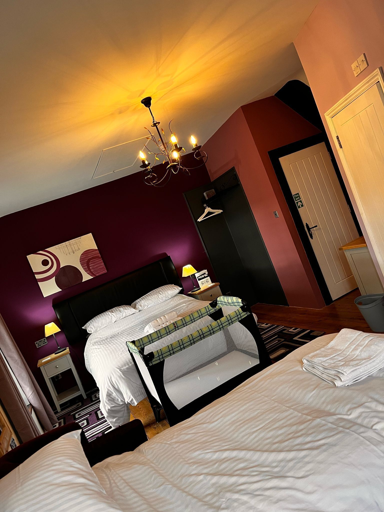 Una camera da letto con un letto, un comodino, una lampada, un lampadario, una porta e una parete con un motivo geometrico.