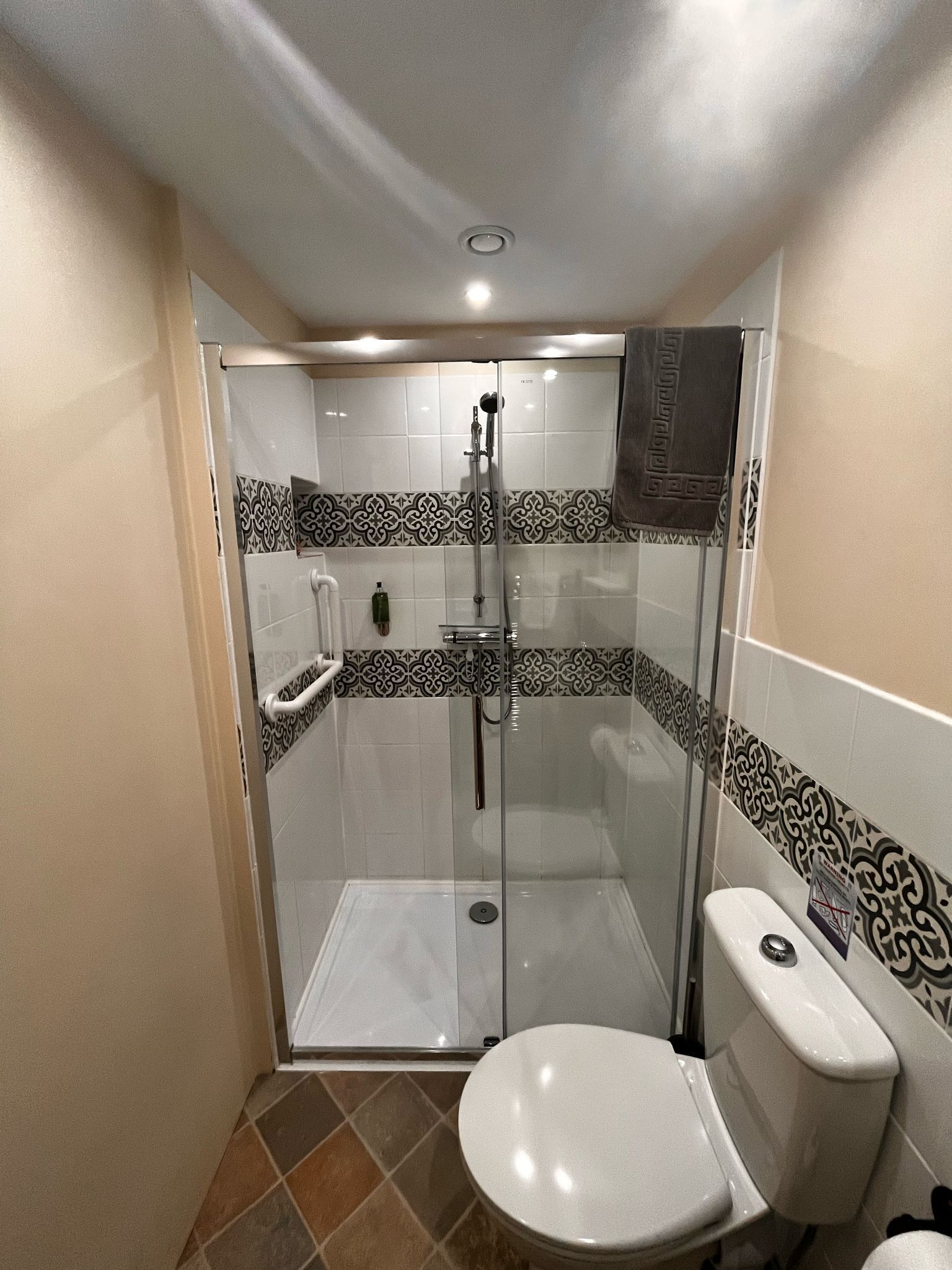 A small, modern bathroom with a glass-enclosed shower, a white toilet, and patterned tiles.