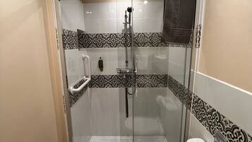 Ein kleines, modernes Badezimmer mit einer gläsernen Dusche, einer weißen Toilette und gemusterten Fliesen.