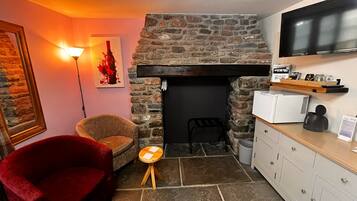 A cozy living area with a stone fireplace, a red armchair, a small wooden stool, and a kitchen area with a microwave and coffee maker.