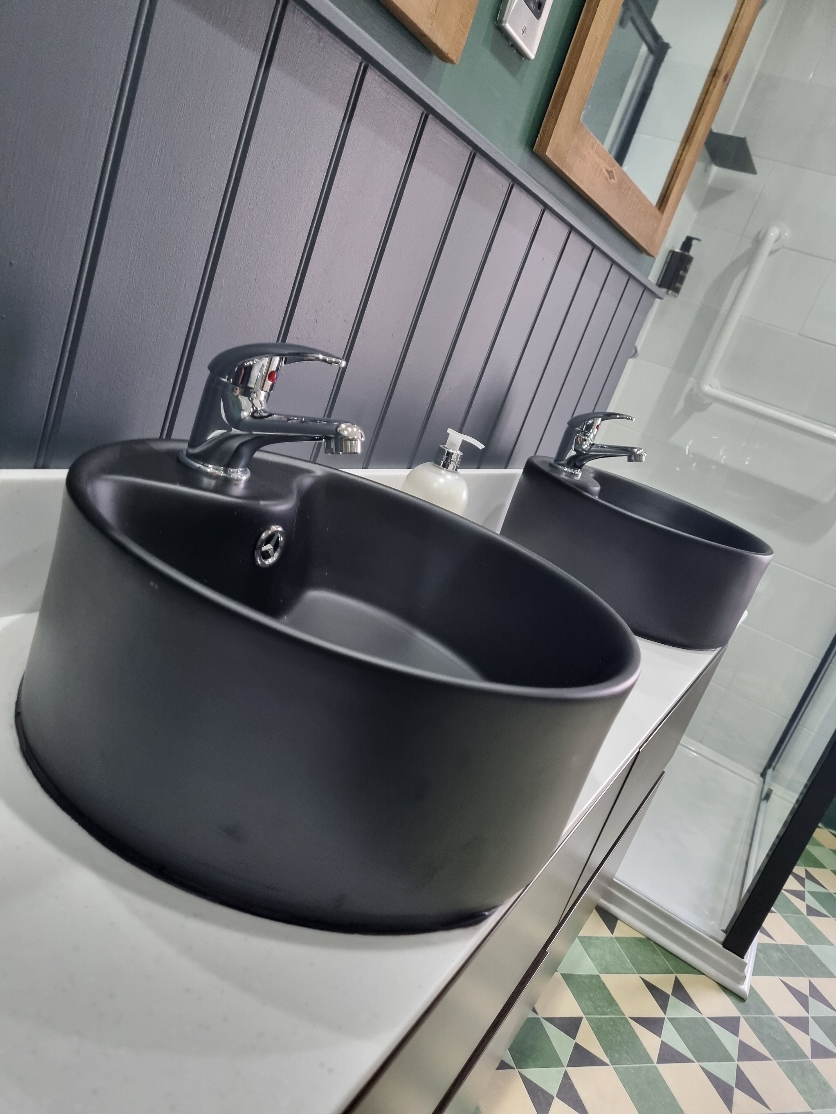 A bathroom with two black sinks, a mirror, and a tiled floor.