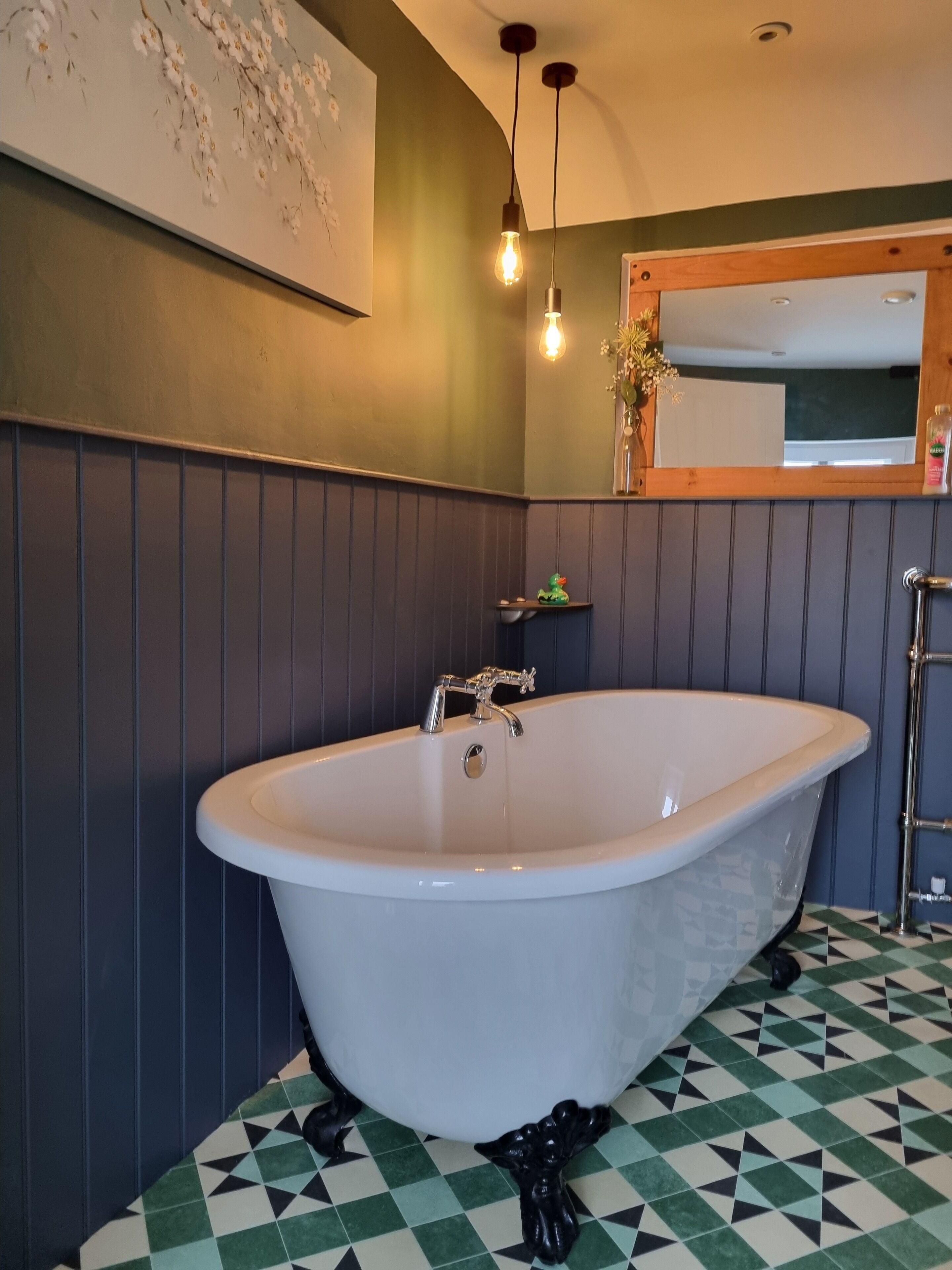 A bathroom with a freestanding bathtub, a mirror above the tub, and a wall-mounted light fixture.