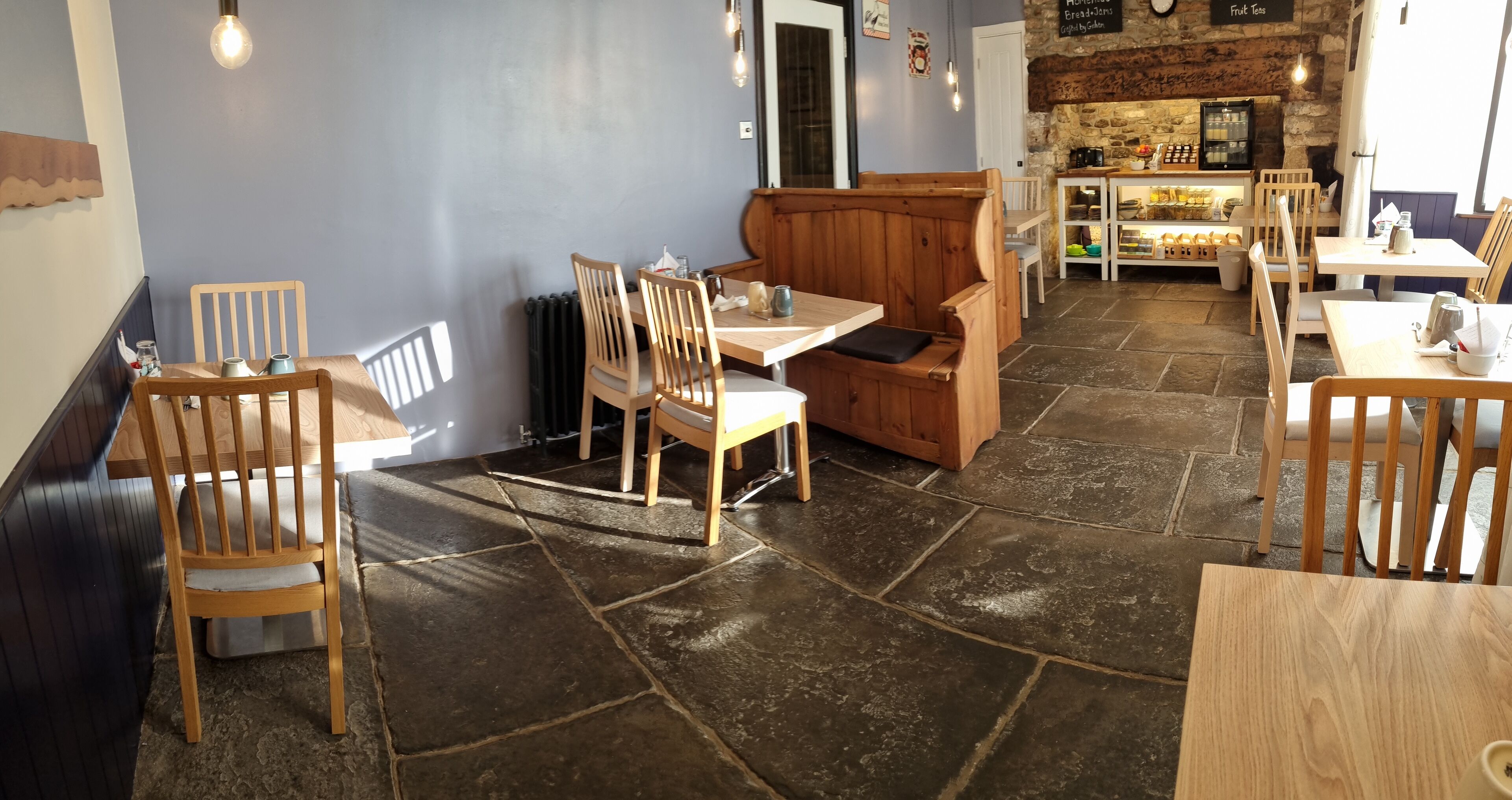 Un acogedor interior de restaurante con mobiliario de madera, suelo de piedra y una pared de piedra.