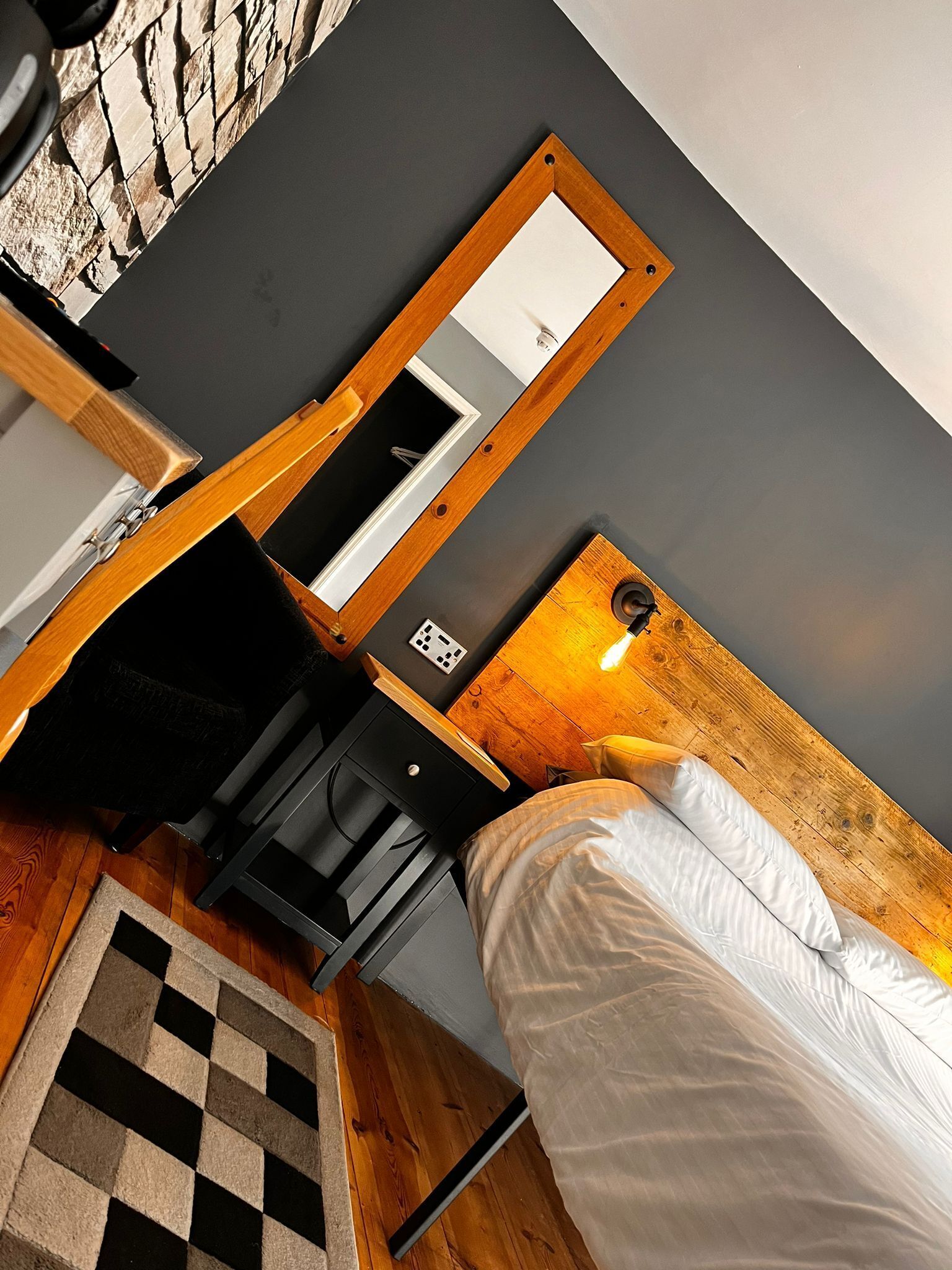 A bedroom with a bed, a wooden headboard, a nightstand, a mirror, and a small desk with a lamp.