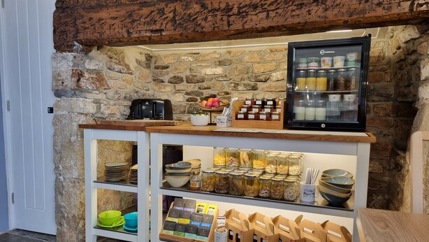 A breakfast bar with a stone wall backdrop, a coffee machine, and a refrigerator stocked with beverages.