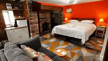 A bedroom with a bed, a sofa, a fireplace, and a nightstand with lamps.