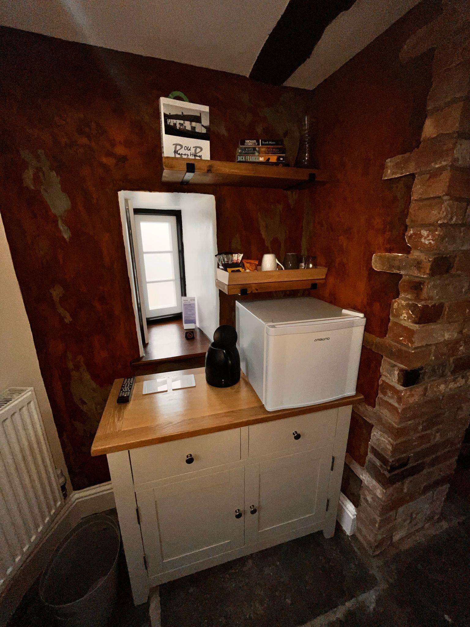 Cocina compacta con refrigerador, cafetera y repisa con libros.
