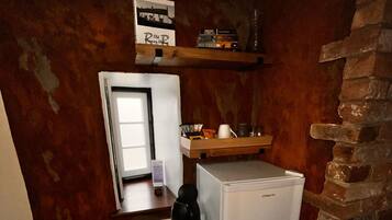 Cocina compacta con refrigerador, cafetera y repisa con libros.