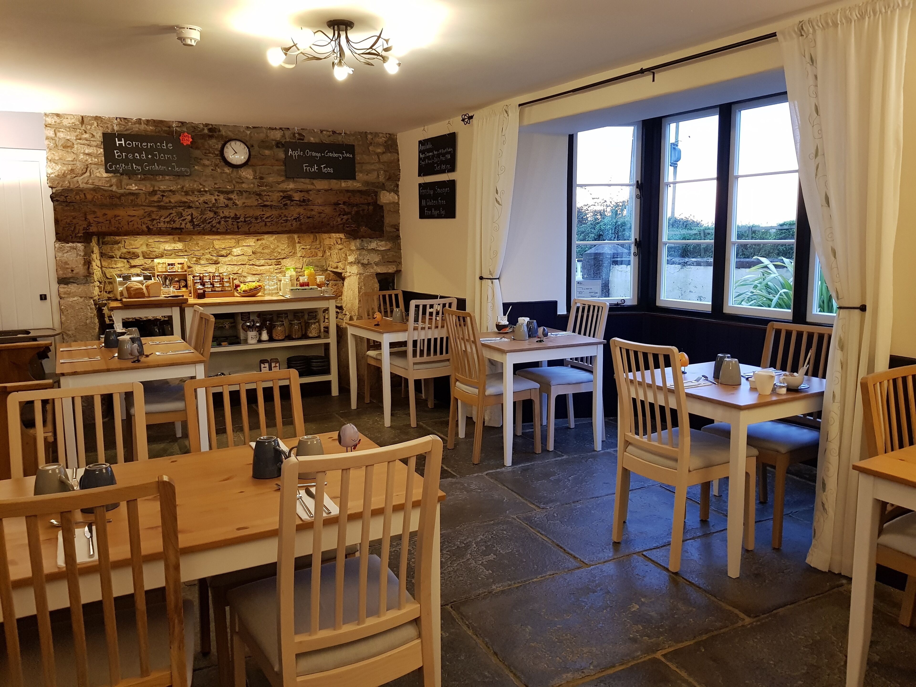 A cozy cafe with wooden furniture, stone walls, and a large window offering a view of the outdoors.