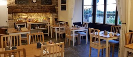 A cozy cafe with wooden furniture, stone walls, and a large window offering a view of the outdoors.