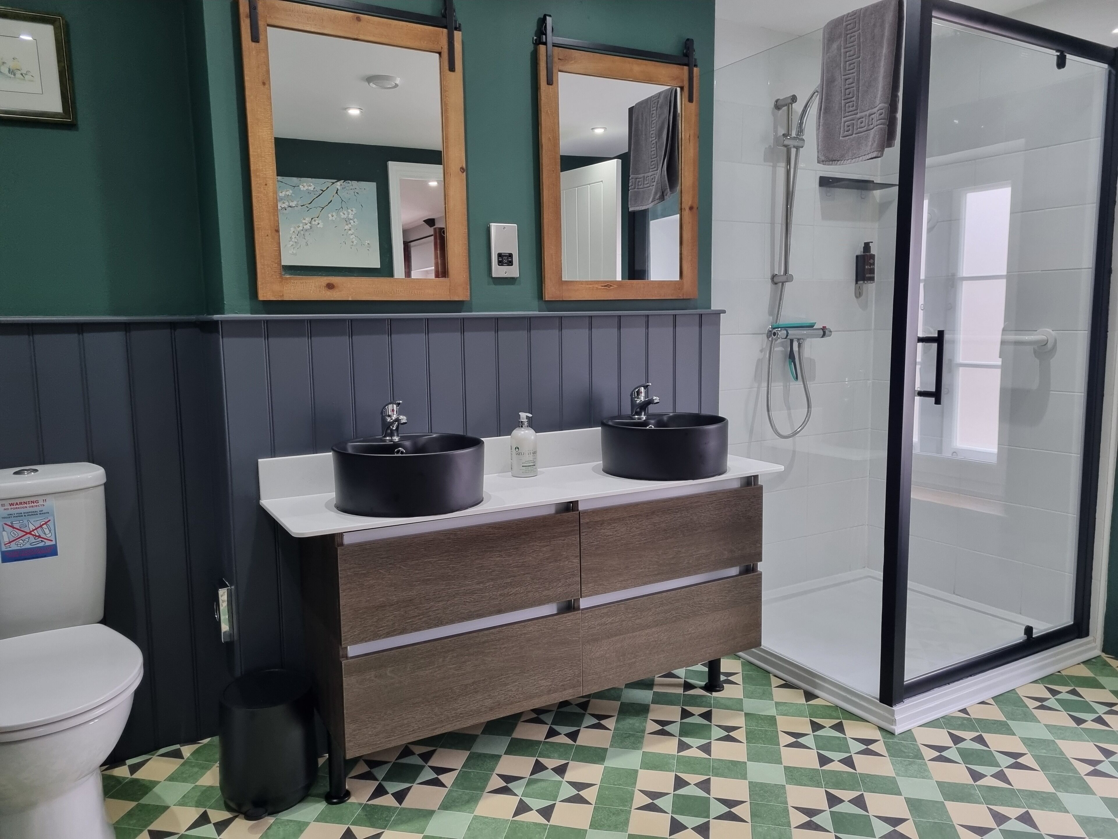 A bathroom with two sinks, a toilet, a shower, and a patterned floor.
