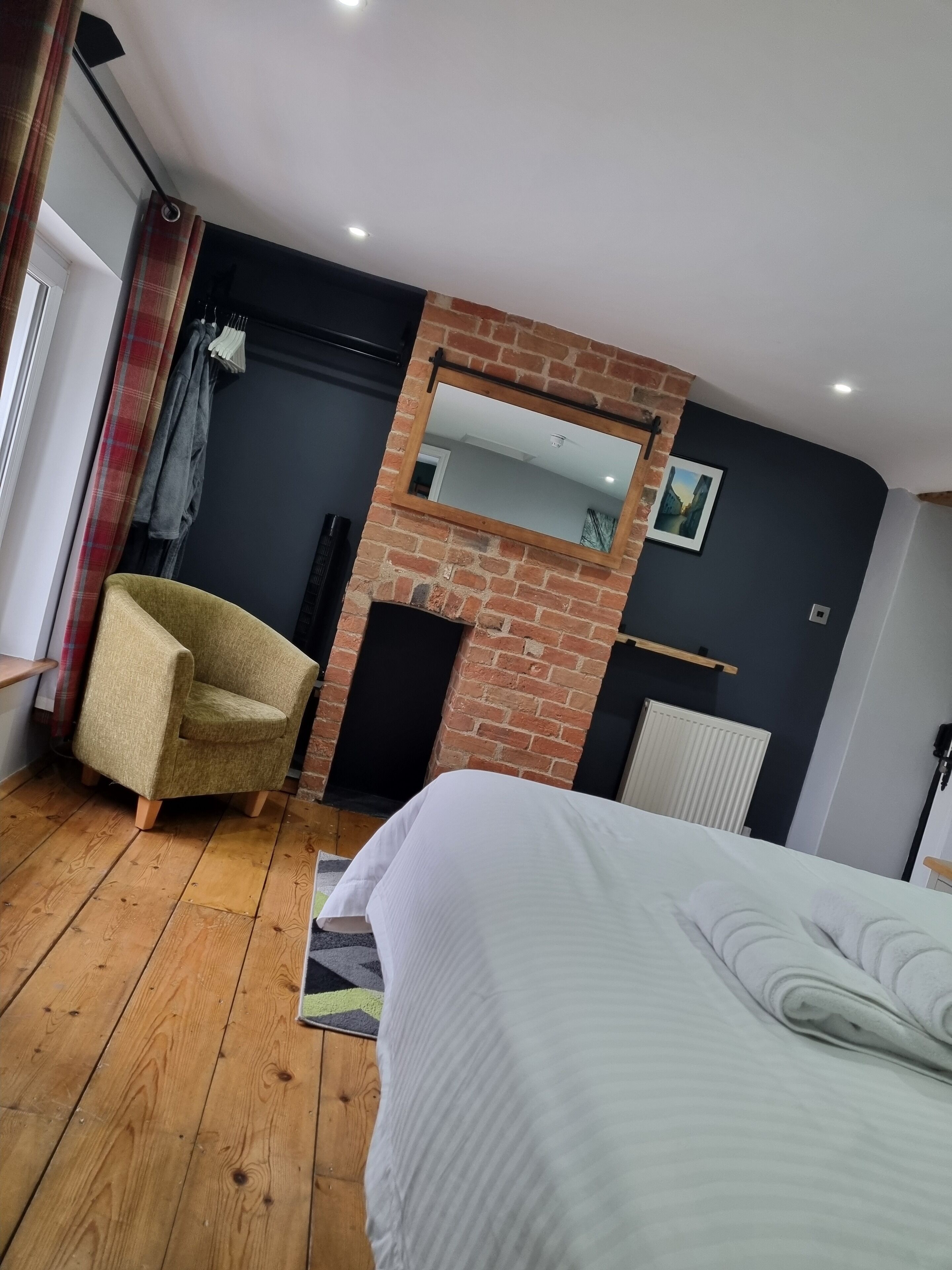 Un dormitorio con chimenea de ladrillo, una cama, una silla y una ventana con cortinas.