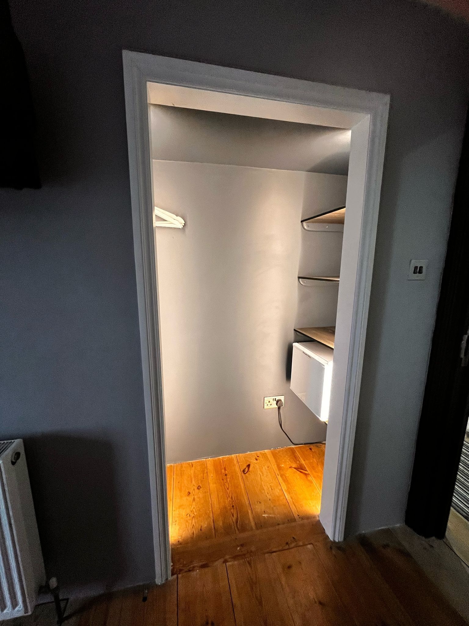Un couloir étroit, doté d’un plancher en bois, mène à une pièce dont la porte est blanche.